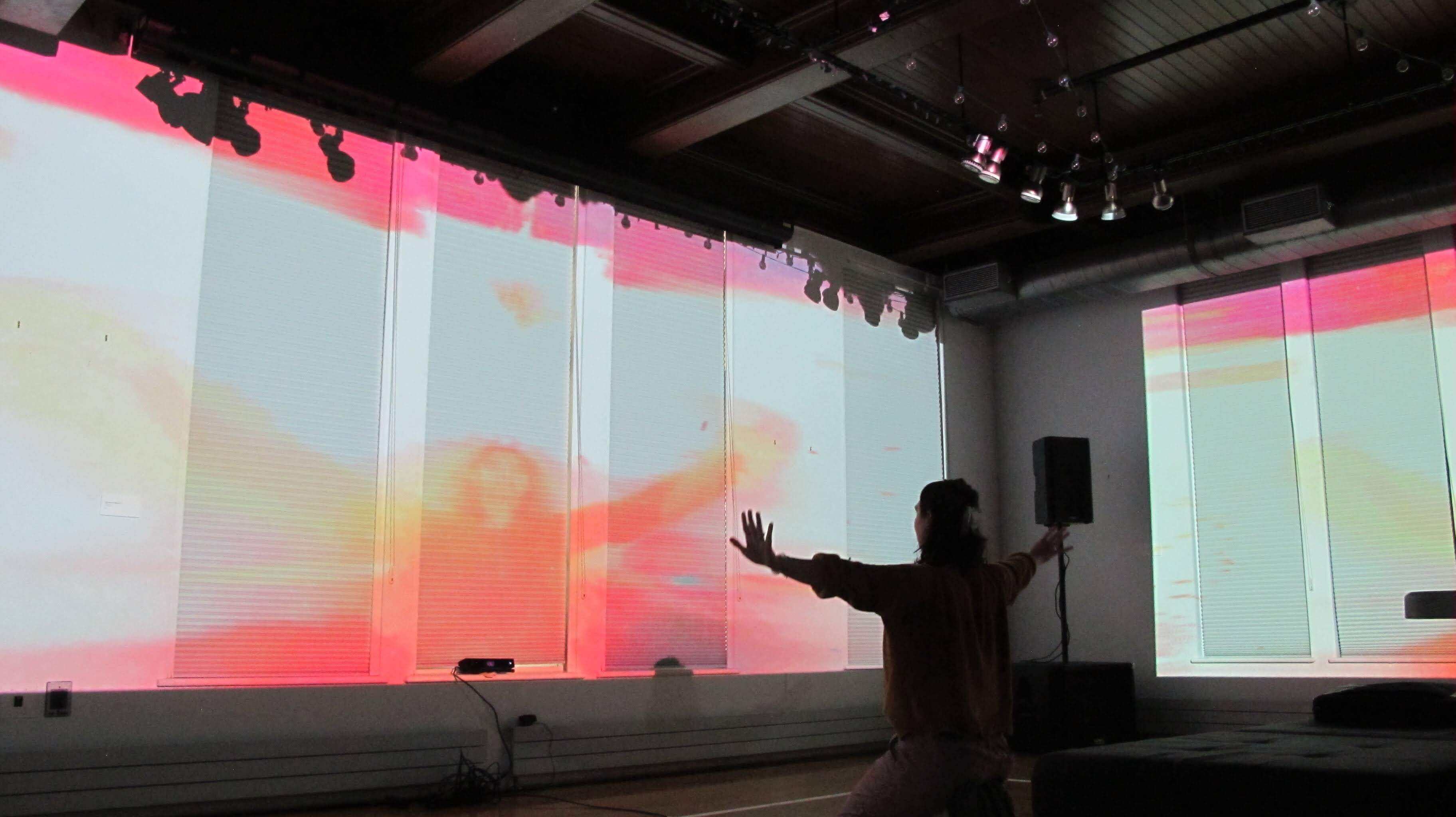 Image of people dancing in front of a large projection. The projection is a colorful abstract pattern that changes with the movement of the dancers. The dancers are silhouetted against the projection, creating a striking contrast.