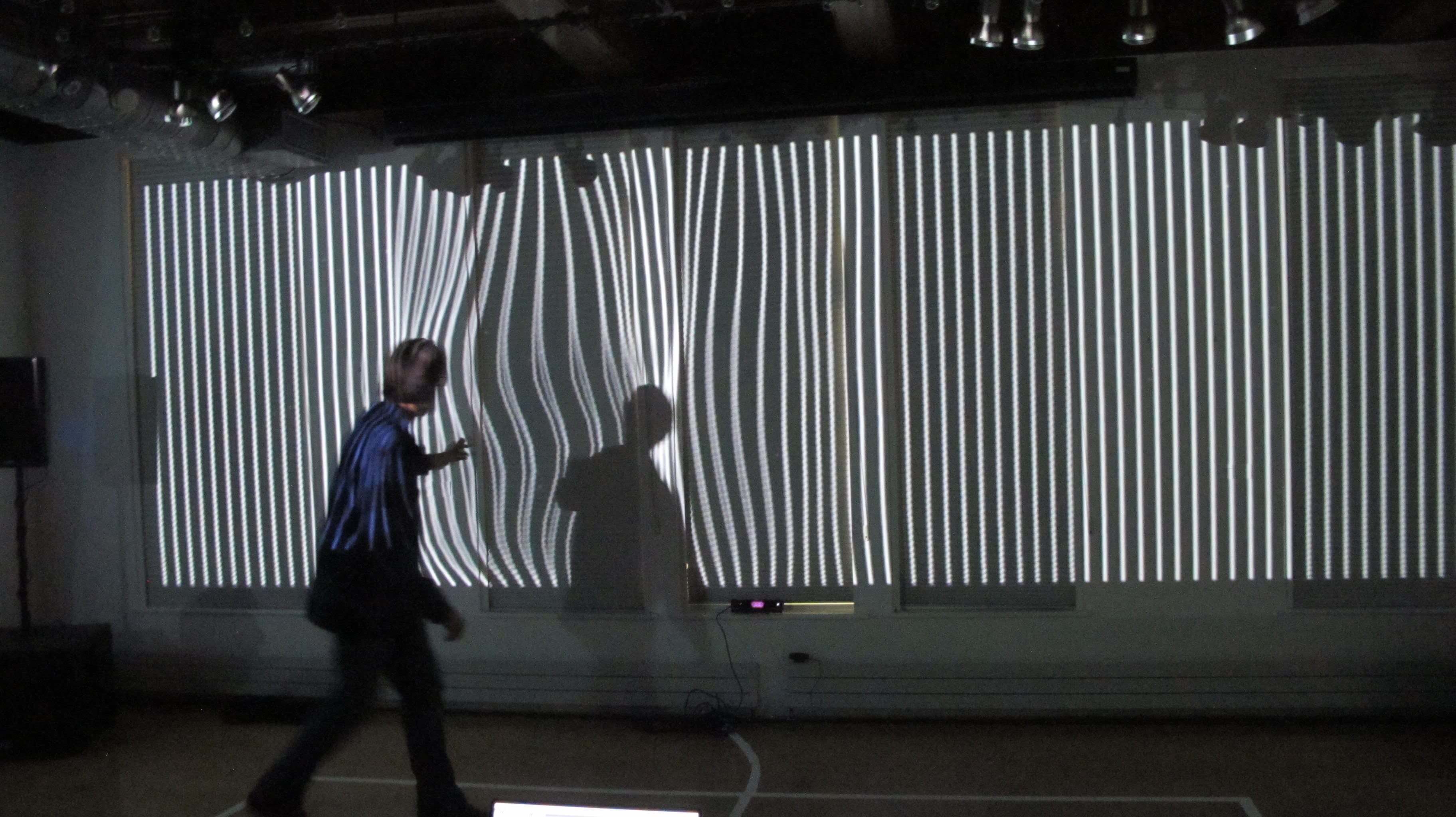 Image of people dancing in front of a large projection. The projection is a colorful abstract pattern that changes with the movement of the dancers. The dancers are silhouetted against the projection, creating a striking contrast.